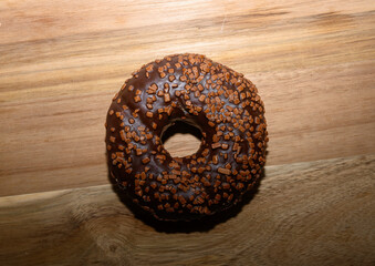 A delectable chocolate donut adorned with crunchy topping sits on a wooden surface, inviting sweet cravings during an afternoon snack break at home