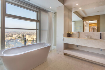 Stylish bathroom design in pastel colors. An elegant bathtub by the window with a delightful panoramic view of the city.