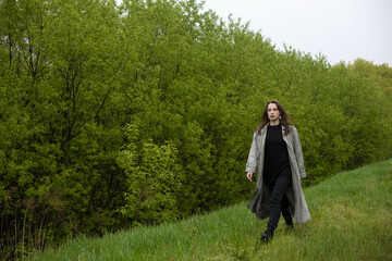 young woman in coat in spring greenery, trees and grass in nature