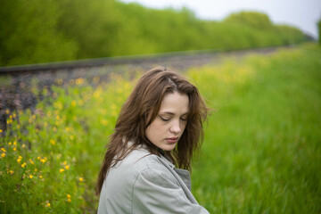 young woman in coat in spring greenery, trees and grass in nature