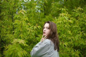 young woman in coat in spring greenery, trees and grass in nature