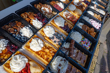Variety of fresh baked waffles richly decorated with different toppings, sweet sweets, chocolate, cream, fruit and berries, jelly sweets in bakery with confectionery shop, old Volendam, Dutch sweets