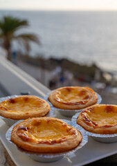 Portugal's traditional sweet dessert Pastel de nata egg custard tart pastry in cup and Atlantic Ocean on background