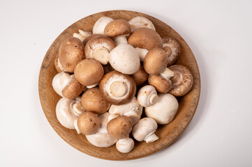 White and brown champignons mushrooms fresh uncooked on wooden plate copy space on white background