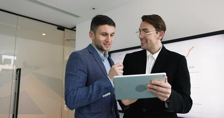 Two young business leader men using tablet for work discussion, analyzing financial strategy, investment plan on stock market, discussing data, online information, smiling - Powered by Adobe