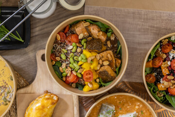 Overhead close-up of a vibrant poke bowl featuring quinoa, spinach, mango, cherry tomatoes, edamame, peanuts, and glazed salmon chunks. Artisanal takeout dish, compostable food box.