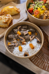 A hearty meal of meatballs in creamy mushroom sauce served with white rice and pumpkin cubes. Vertical close-up shot on wooden table, Fast-casual dining experience, sustainable takeaway packaging.