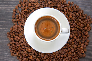 Fototapeta premium A classic white espresso cup and saucer hold a rich, frothy coffee, framed by a bed of roasted coffee beans, highlighting the essence of a perfect morning brew