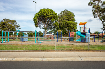 A fenced suburban playground features climbing structures, slides, and monkey bars in Australia....