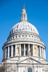 Obraz premium St. Paul's Cathedral in London features its impressive dome, showcasing intricate architecture against a clear blue sky. The iconic structure attracts many visitors throughout the day.