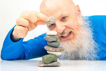 Enthusiastic older man smiling widely while engaged in building a stack of assorted stones,...