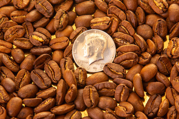 Roasted coffee beans with a U.S. dime for scale on a golden reflective background, showcasing their...