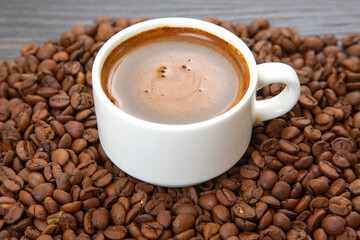 Dark espresso with a velvety crema fills a white cup on a saucer, surrounded by whole coffee beans, creating a cozy and aromatic coffee-themed composition