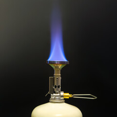 Close-up of a portable camping stove with a vibrant blue flame burning brightly against a black...