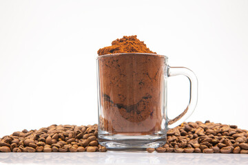 A detailed shot featuring a glass mug packed with coffee powder, encircled by whole roasted coffee beans, perfect for coffee lovers and culinary themes