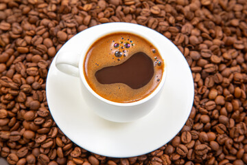 Top-down view of a white espresso cup with dark coffee and crema, placed on a matching saucer, surrounded by roasted coffee beans on a textured brown background