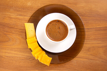Obraz premium minimalist setup showcasing a steaming espresso in a white cup on a saucer, paired with neatly arranged yellow cheese slices, set against a rustic wooden background.