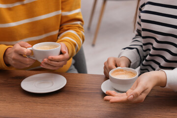 Coffee break. Women with cups of hot drinks at wooden table indoors, closeup
