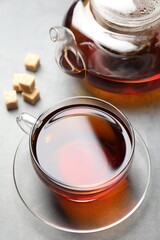 Aromatic black tea and brown sugar cubes on light grey table, closeup