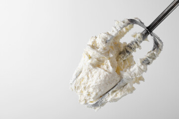 Whisk with whipped cream on white background, closeup. Space for text