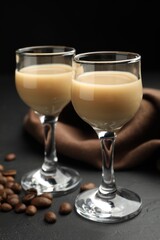 Coffee cream liqueur in glasses and beans on black table, closeup