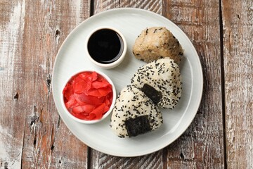 Rice balls (onigiri), soy sauce and pickled ginger on wooden table, top view. Traditional Japanese dish