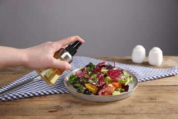 Woman with bottle of oil and salad at wooden table against grey background, closeup