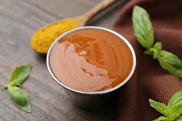 Tasty curry sauce in metal dish, powder and basil on wooden table, closeup