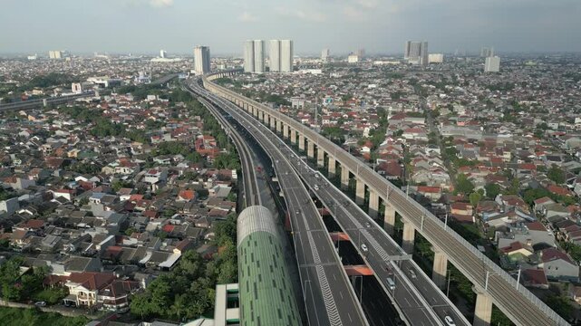 Aerial view of LRT commuter train passing through elevated tracks above highway and urban neighborhood in Jakarta, Indonesia.