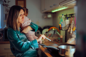 Busy Mom Holds Baby While Preparing Meal in Kitchen. Tired mother struggles to cook with the baby in her arms