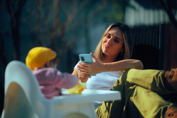 Mother Checking her Phone While Baby Eats by Itself. Mom distracted by her smartphone during meal time of her little one