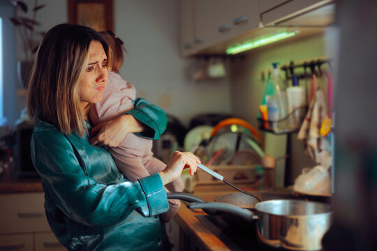 Busy Mom Holds Baby While Preparing Meal in Kitchen. Tired mother struggles to cook with the baby in her arms