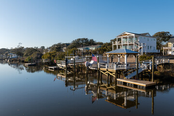 OAK ISLAND, NC, USA - March 12, 2025: Docked boats reflect in the still waters of a peaceful canal lined with homes and trees.