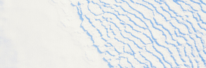 Beautiful winter background with snowy ground. Natural snow texture. Wind sculpted patterns on snow surface. Wide panoramic texture for background and design.