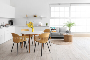 Interior of light spacious kitchen studio with dining table, mimosa flowers, armchairs, houseplant, counters and sofa