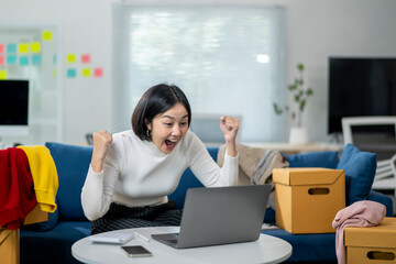 A woman is sitting on a couch and is excitedly celebrating on a laptop