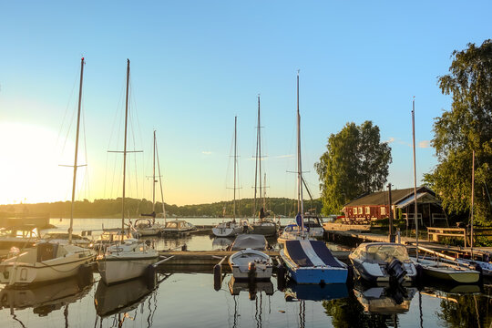 Tranquil small boats marina with sailboats and motorboats in beautiful summer sunset with clear sky reflected in still water - Powered by Adobe