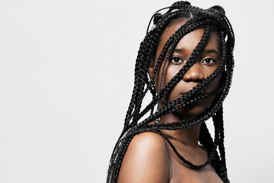 Portrait of a woman with long braided hair against a minimalist white background, showcasing confidence and style, perfect for beauty and fashion concepts