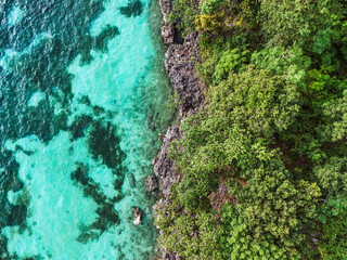 Rocky coastline of a tropical island with clear blue ocean and lush green foliage. Summer vacation and summer holiday concept