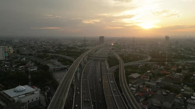Aerial view of highway intersection and train lines at sunset over a dense cityscape in Bekasi, Indonesia.