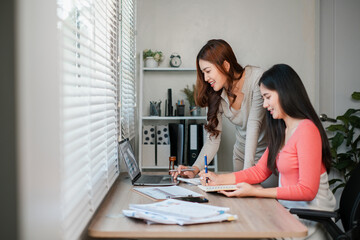 Two women working together in a bright office, using laptops and notebooks, fostering collaboration and productivity.