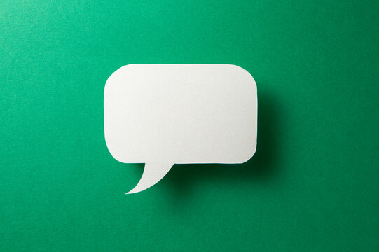Paper speech bubble in the shape of a rectangle on a green background. Flat white chat icon in the form of an empty speech bubble.