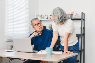 Obraz premium Elderly couple discussing something while working on laptop in home office setting.