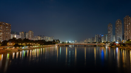 Fototapeta premium A night view of Sha Tin city showing modern high rise housing development on both banks of the Shing Mum River. Hong Kong.
