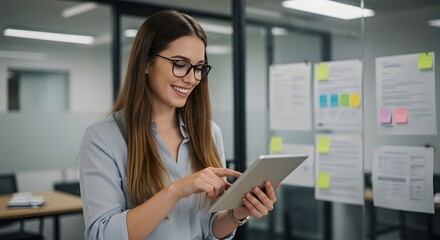 A woman with glasses smiles while using a tablet in a modern office.