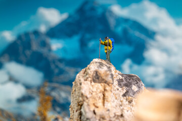 Miniature Climber Reaches Summit Against Majestic Mountain Backdrop