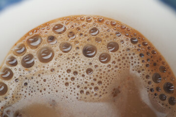 Foam rises above a coffee in a white cup, inviting enjoyment