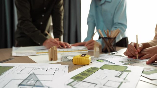 Smart architect and safety engineer discussion about building blueprint on table with architectural document, measurement tools and wooden block scatter around at modern office. Closeup. Delineation.
