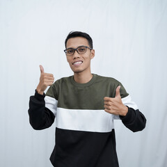 An Asian young man with glasses wearing a sweater smiling expression while giving a thumbs up sign. Isolated on white background.