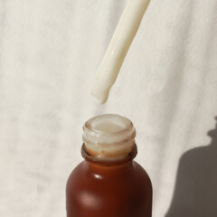 A drop of cosmetic product drips from a pipette into a small brown jar. Facial skin serum. A...